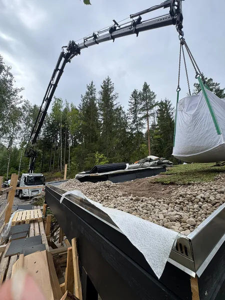 Suursäkki nosturin varassa metsäisen rakennuspaikan yläpuolella.